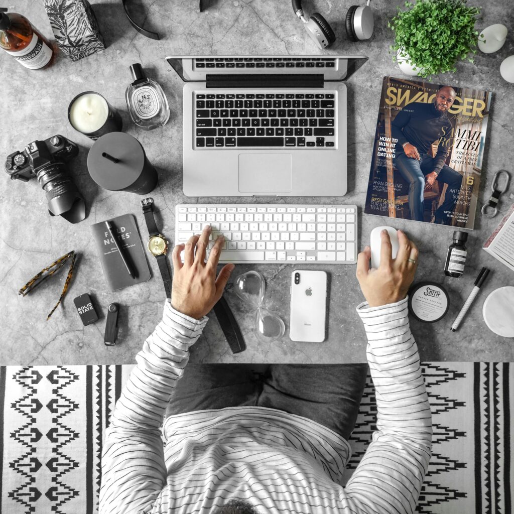 Overhead view of an organized desk with tech gadgets, fashion magazine, and accessories for modern working lifestyle.
